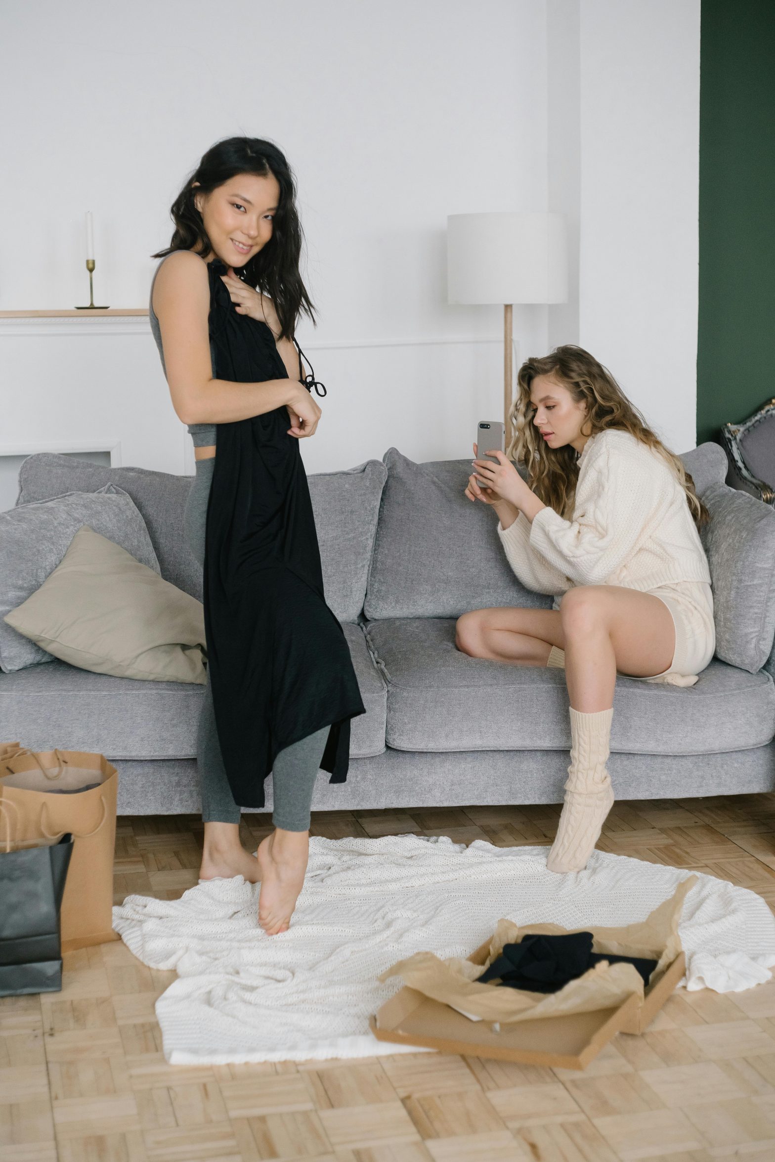 Two women sitting on a gray couch in a well-lit, cozy living room.