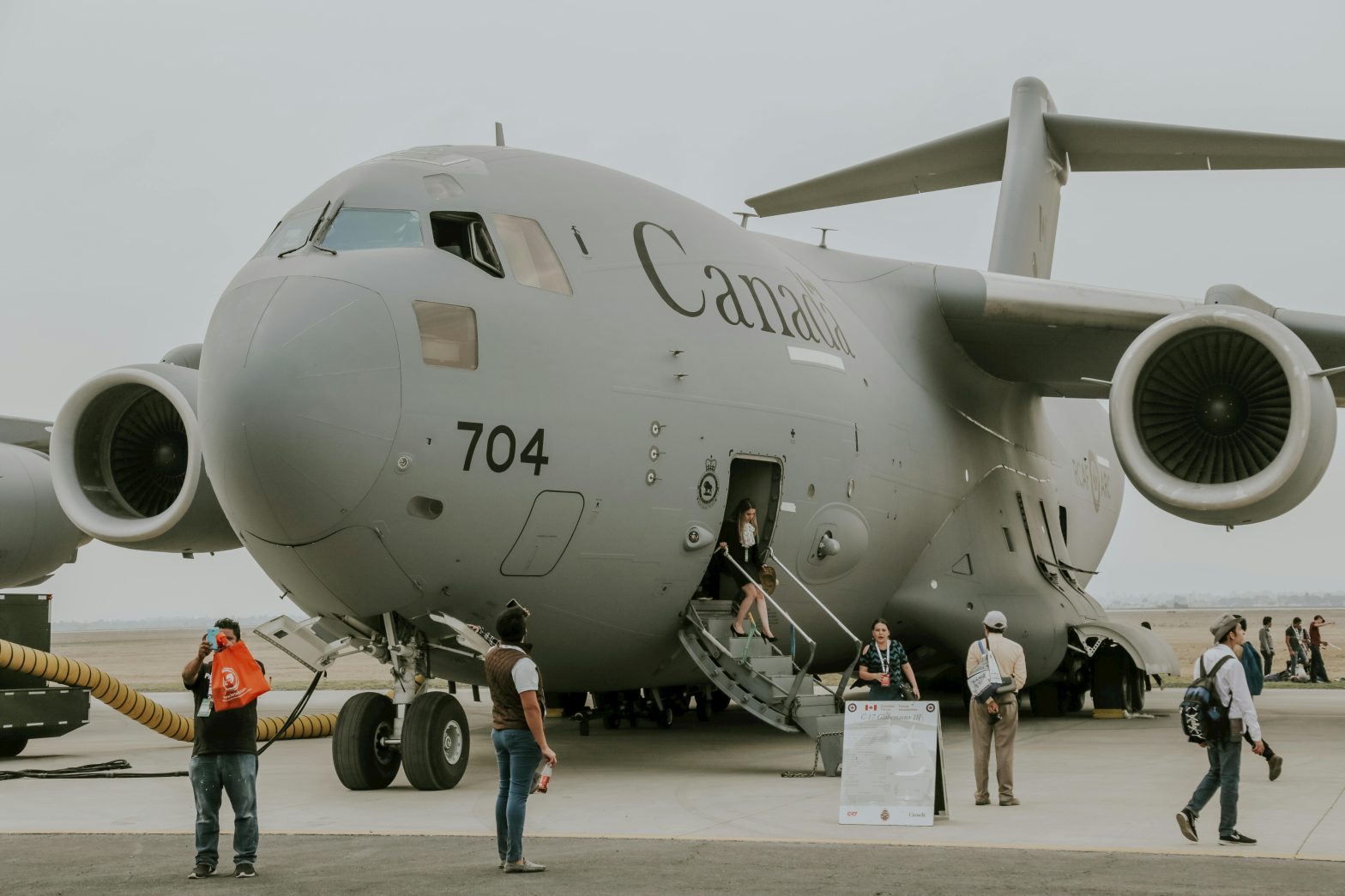 A group of people disembarking from a C-17 military transport aircraft on an airstrip. The image captures the movement of personnel exiting the plane under a partly cloudy sky.